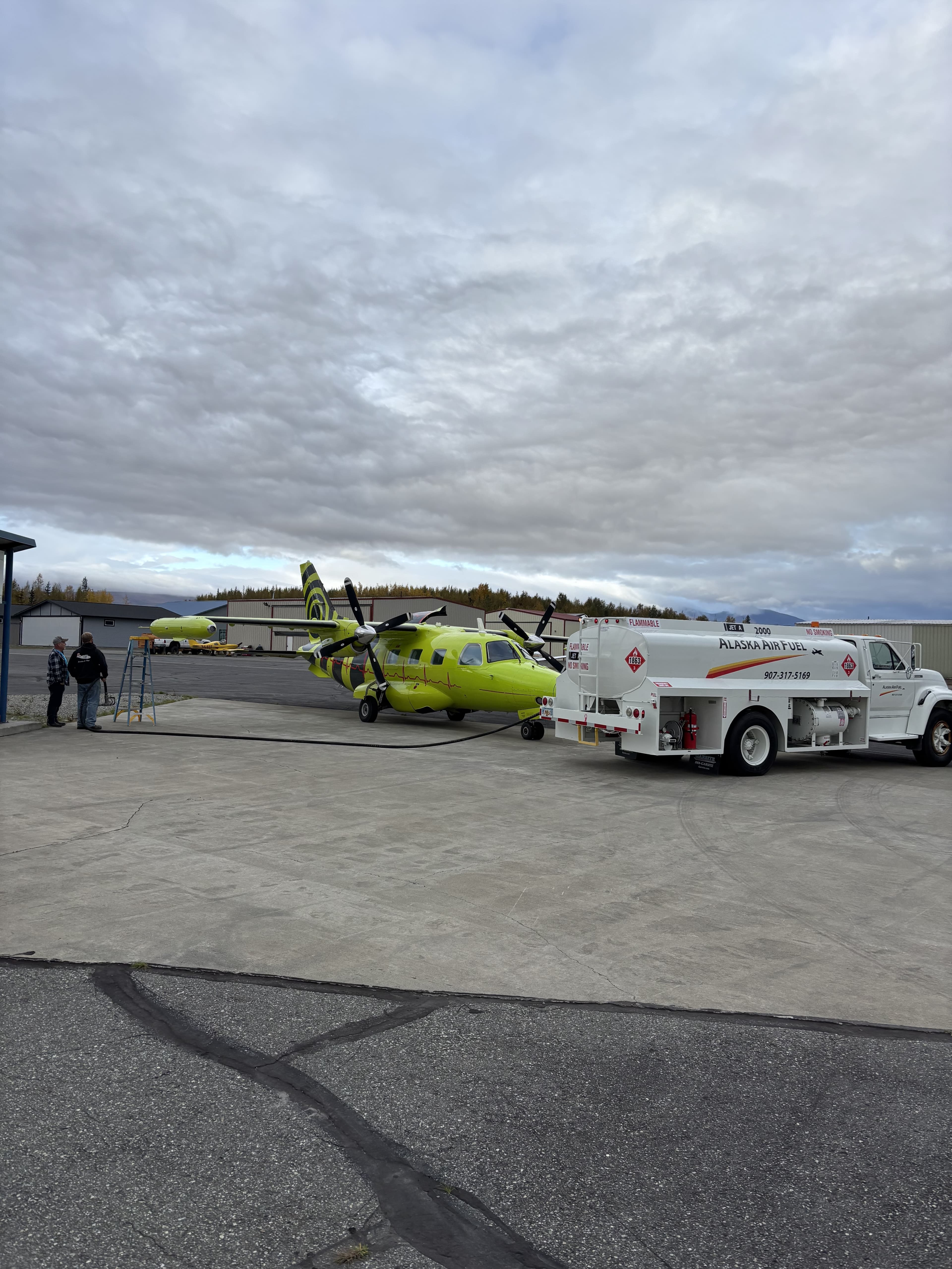Yellow aircraft being fueled by Alaska Air Fuel truck on the ramp
